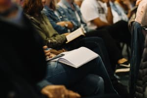 Attendees of a conference or workshop sit in a row with open notebooks on their laps.
