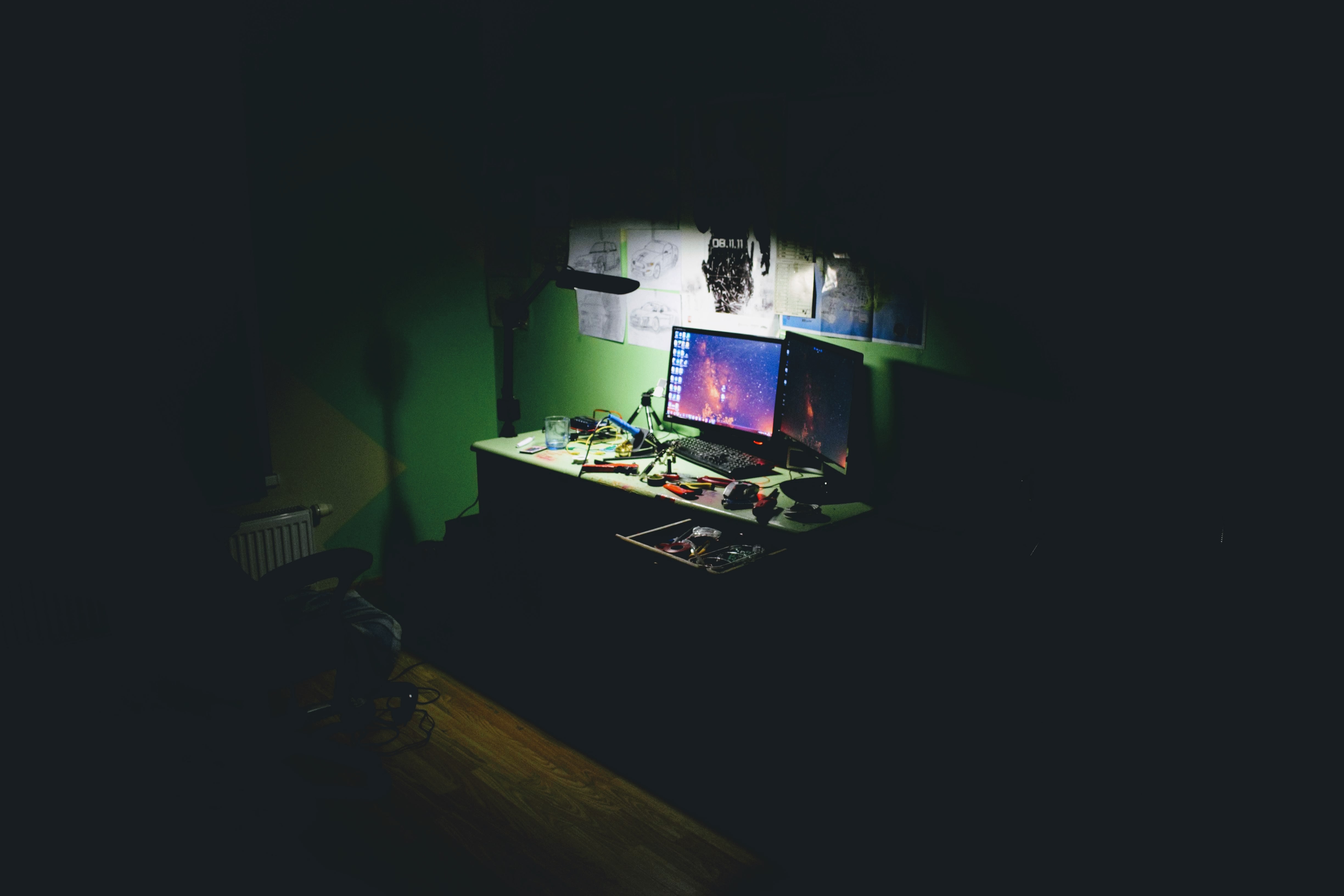 A picture of a dark room with a computer glowing on a desk.
