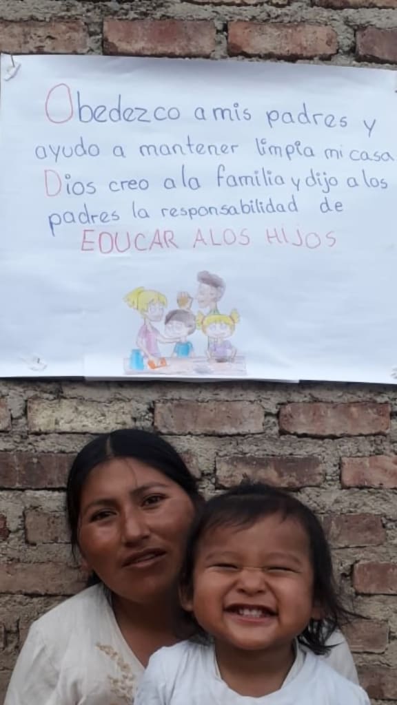 A mother and child smile underneath the banner that they've made.