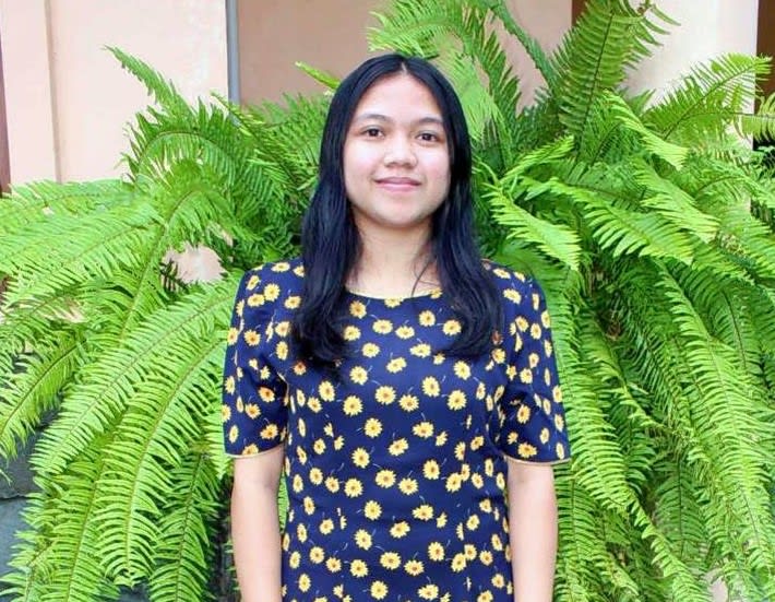 A girl in a blue dress with a yellow flower pattern smiles at the camera