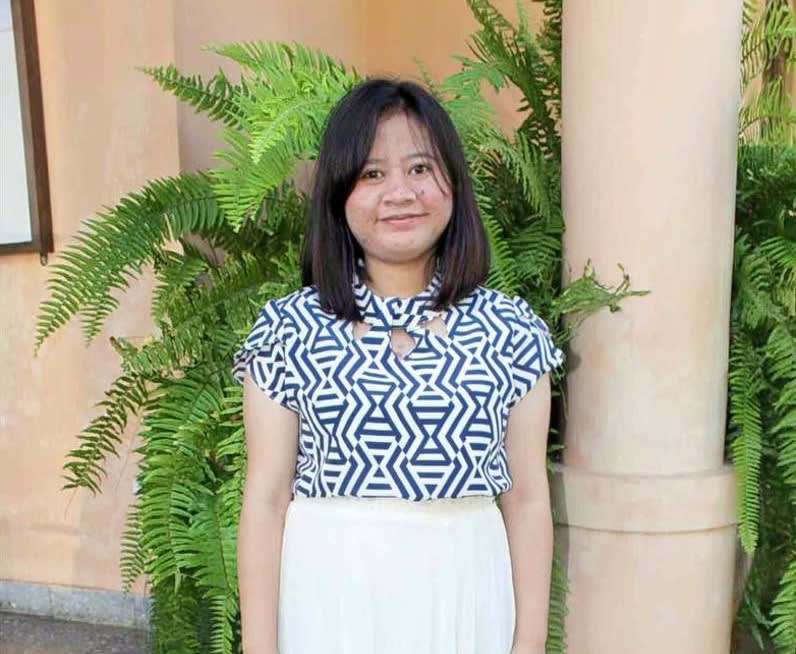 A girl in a patterned top and a white skirt smiles at the camera