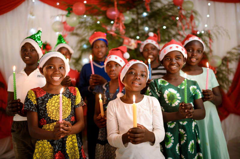 Children from Uganda hold candles and wear festive hats.