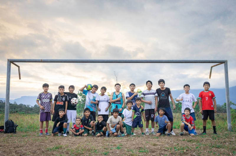 A group of boys pose in front of a soccer goal after their practice. They are smiling at the camera.