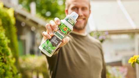 Mann hält eine Flasche COMPO Booster für torffreie Erden in die Kamera