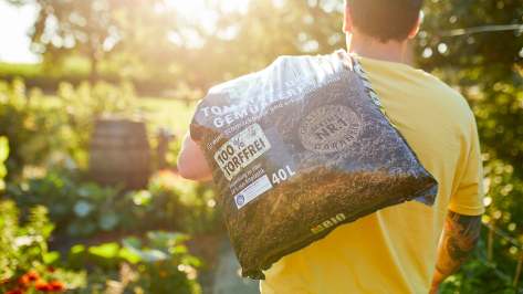 Mann trägt einen Sack COMPO BIO Tomaten- und Gemüseerde torfffrei über der Schulter