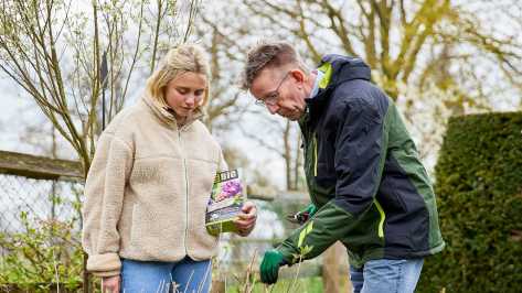 Werner Peitzmann zeigt junger Frau wie man einen Rhododendron schneidet