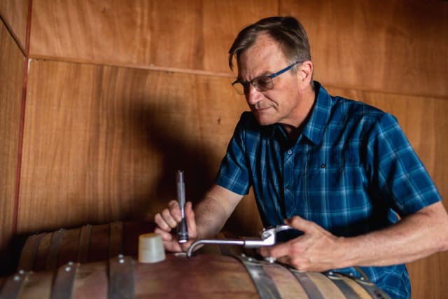 Winemaker David Bellows checking the wine level in a barrel of natural wine.