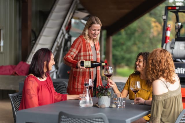 Erin Allen serving Pinot Noir wine to guests seated on the crush pad at one of the best wineries in the Willamette Valley.