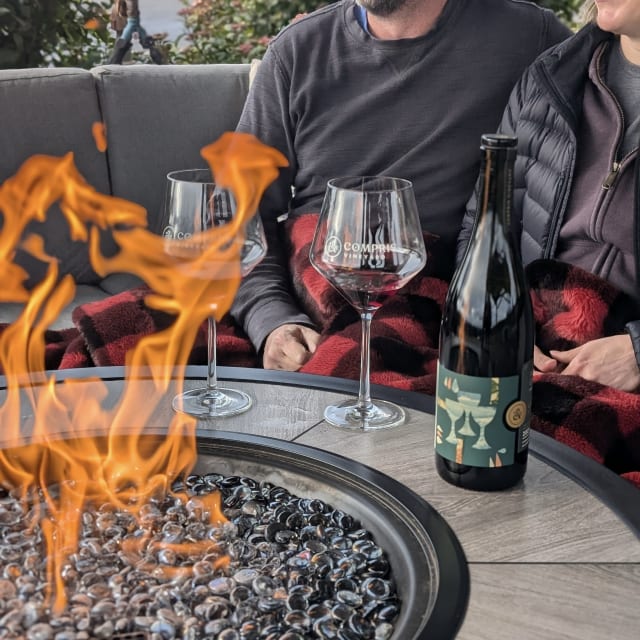 A happy couple at Compris Vineyard in the fall, with the warm fire table glowing, warm blankets, and glasses of Pinot Noir.
