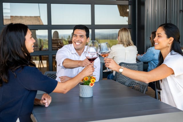 Slide Image. A group of three enjoying their wine tasting on the covered patio of Compris Vinyeard.