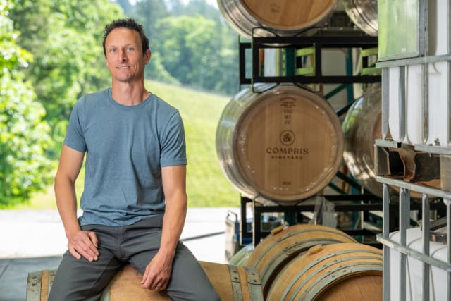 Winemaker Aaron Kendall with barrels inside of the production space -  he enjoys practicing sustainable farming and making organic wine.