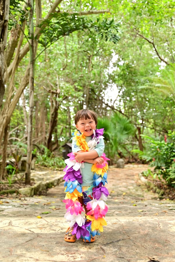 A boy around 4-years old  with a colorful lei smiles