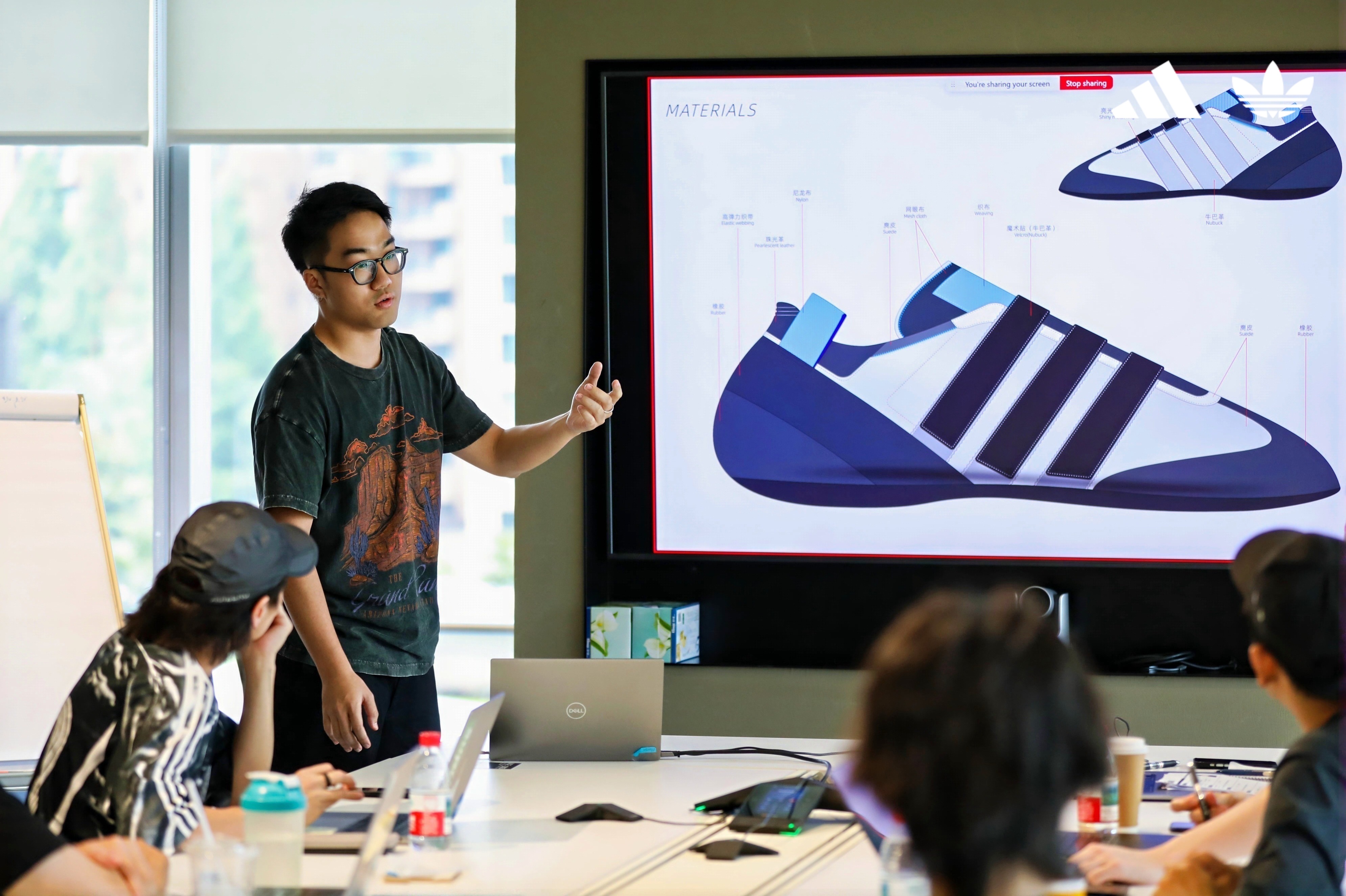 A young man presents a shoe design on a screen to other students in the room