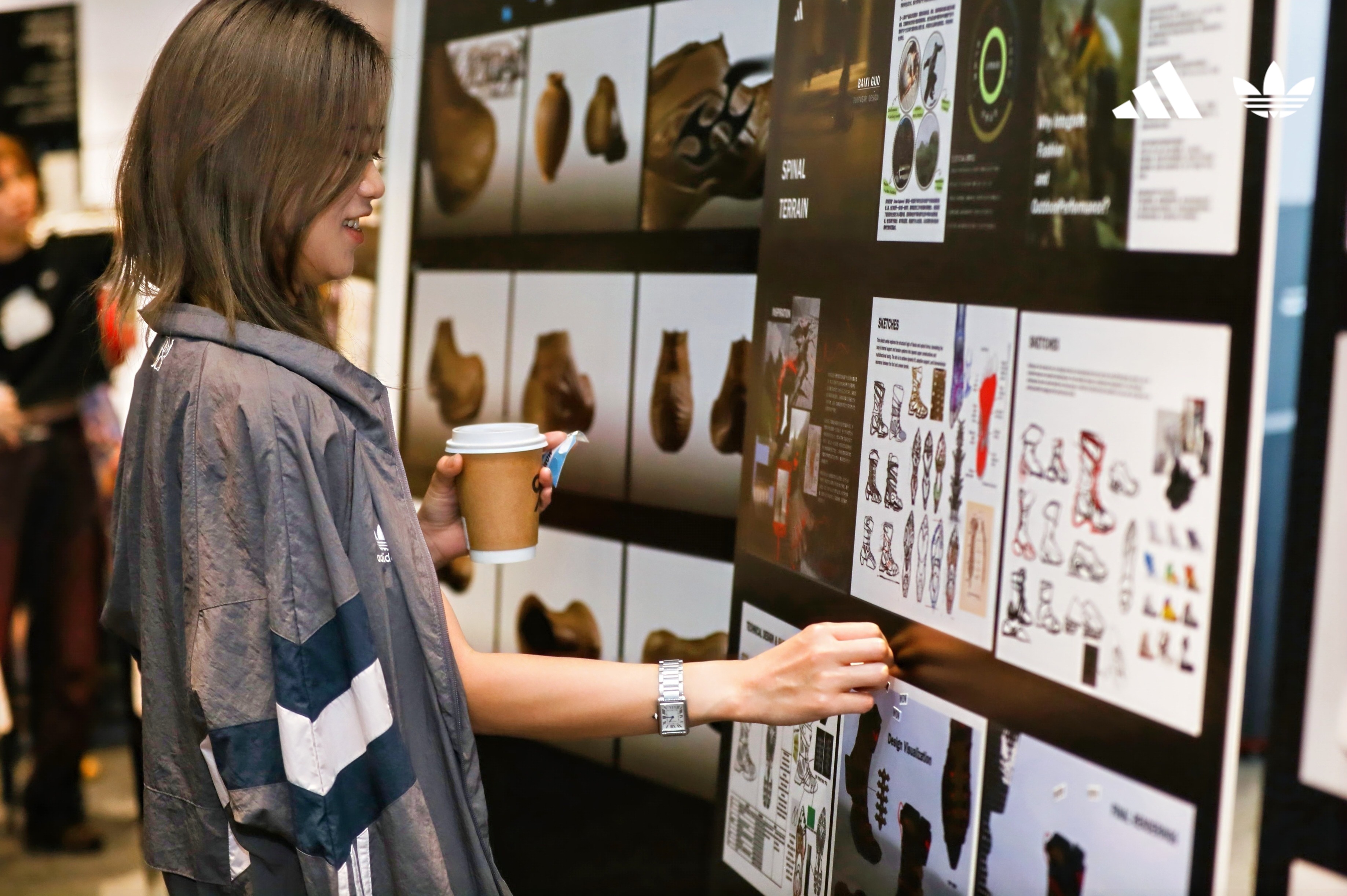 A young woman holding a cup of coffee adds her vote to a design on a display board
