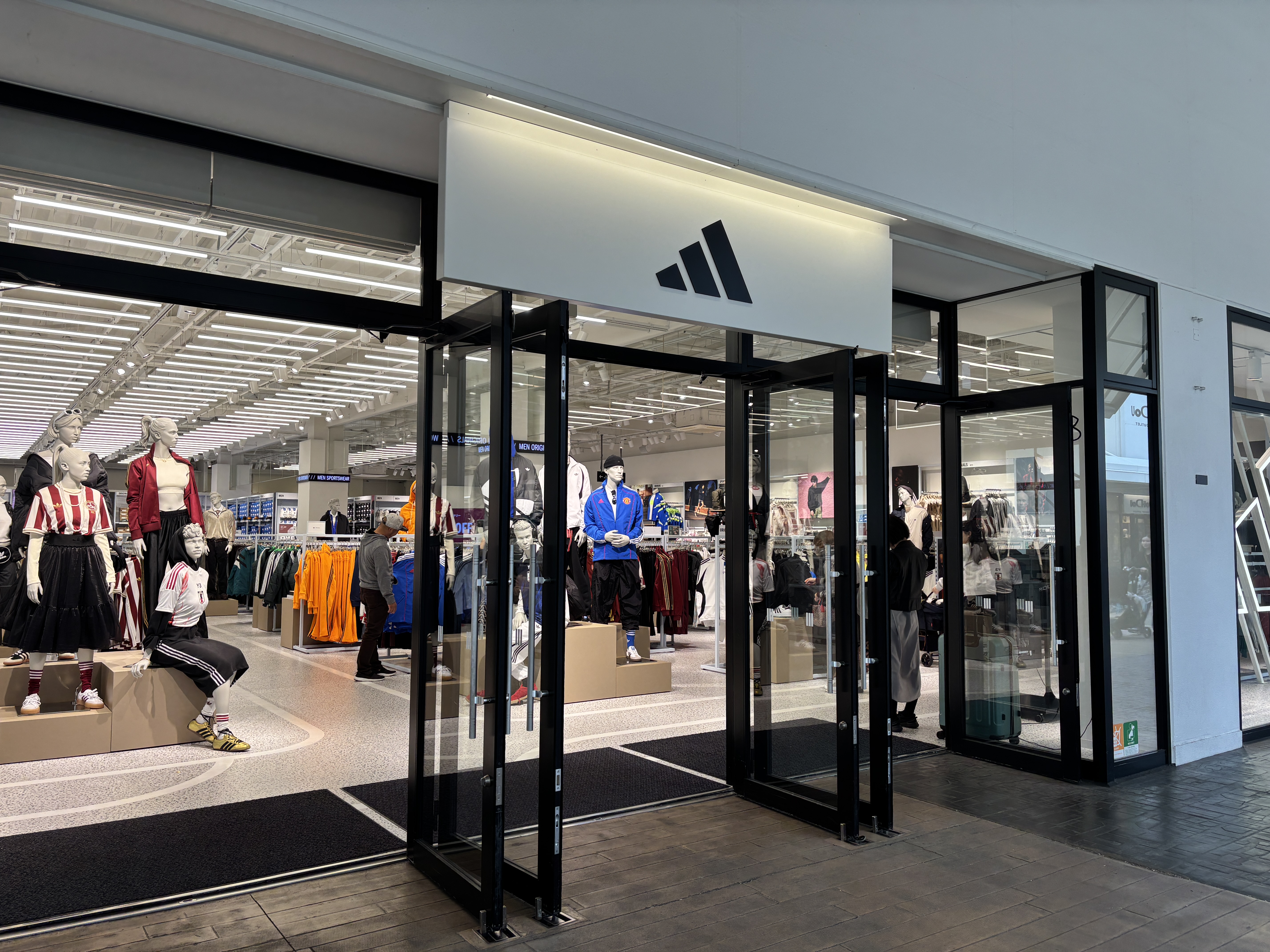 Entrance of an adidas store with colorful apparel showing through the windows