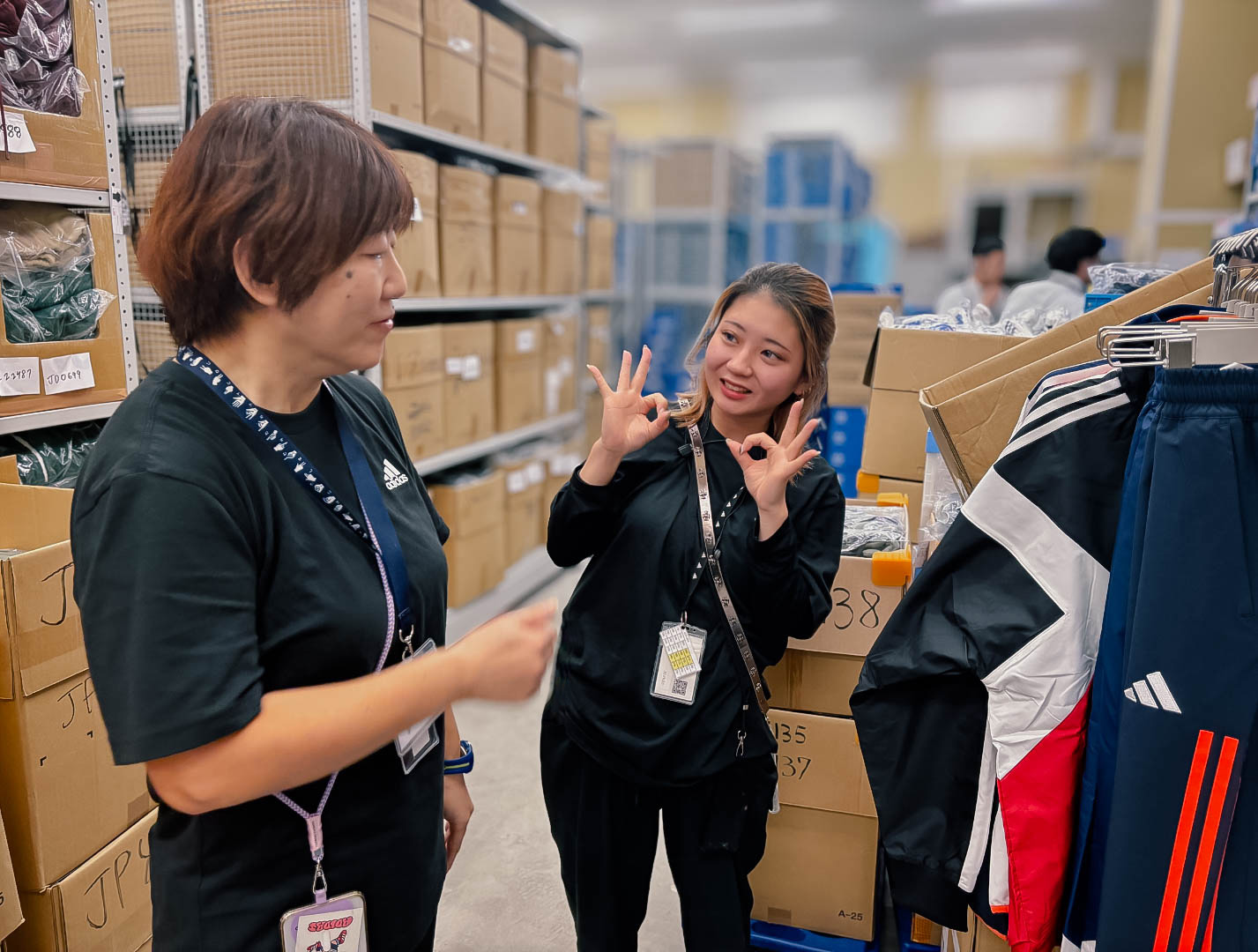 Two woman stand in a store, one using hand gestures to communicate with the other.
