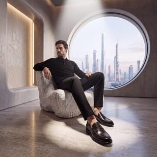 uomo vestito in nero con mocassini pierre cardin seduto su una poltroa