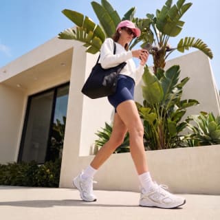 La foto mostra una ragazza con uno stile sportivo ma casual che cammina per la città. Indossa un paio di new balanca retro running, shorts in tessuto e una felpa.