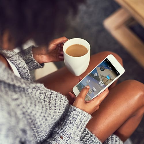 Woman drinking coffee while she uses the Control4 Mobile App to manage the devices in her home