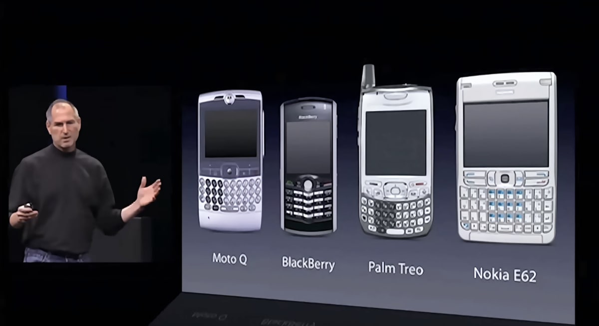 Steve Jobs presenting a slide comparing the smartphones of the day: Moto Q, BlackBerry, Palm Treo and Nokia E62.