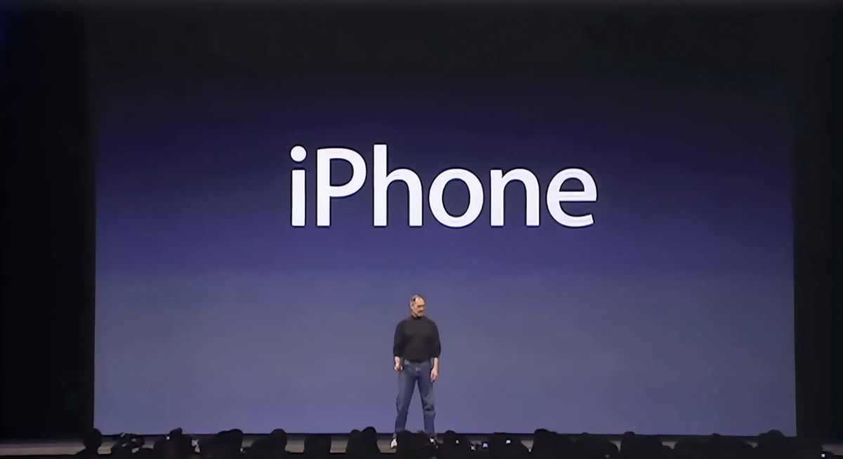 Steve Jobs alone on a vast stage as the word &lsquo;iPhone&rsquo; fills the screen behind him.