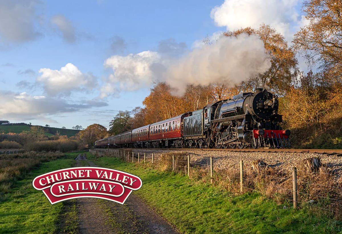 A green tank engine pulling maroon carriages under a plume of white steam through autumn woodland on the Churnet Valley Railway.