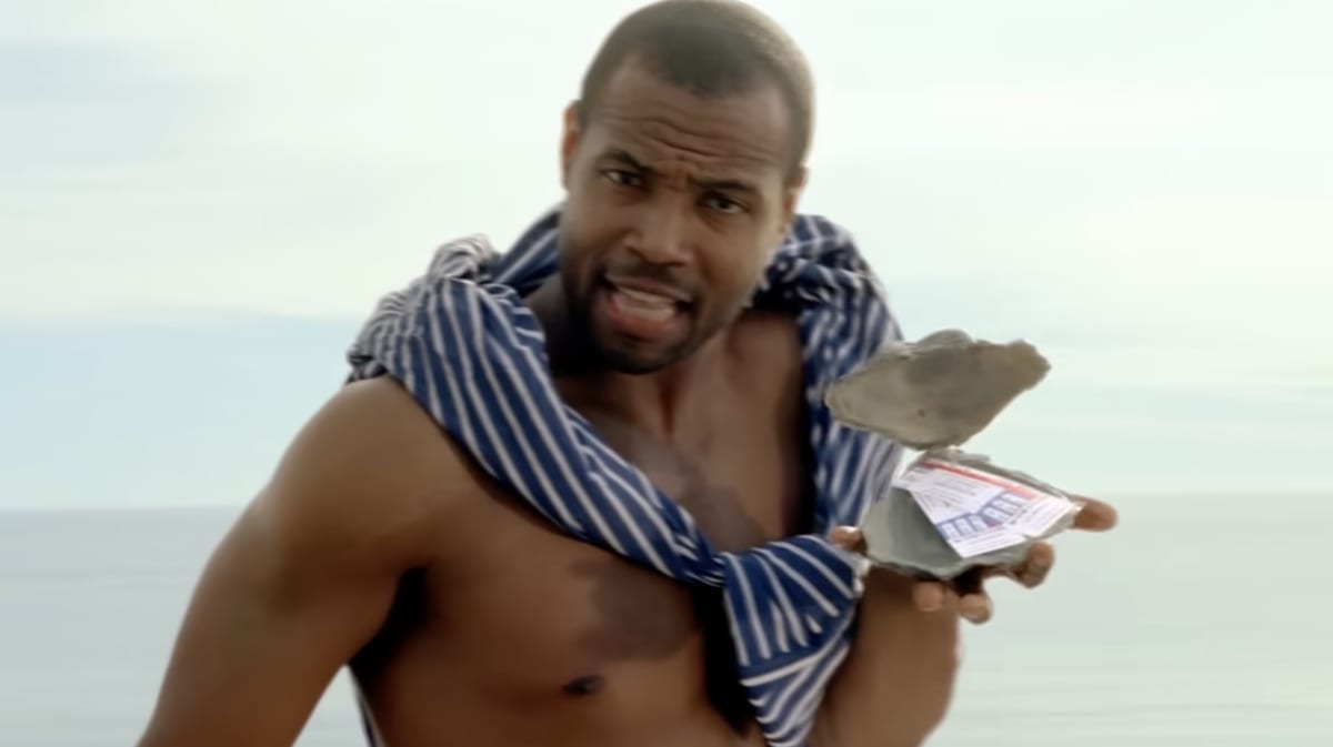 Isaiah Mustafa on the beach holding open an oyster shell containing two tickets, from the line ’it’s an oyster with two tickets to that thing you love.’