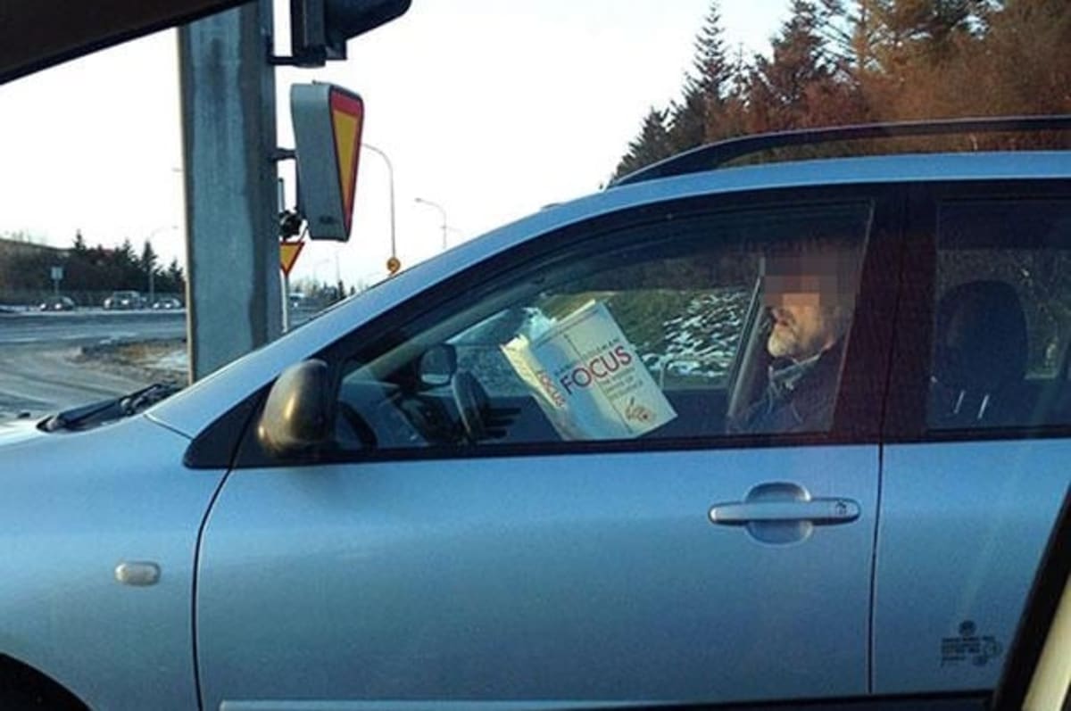 Man reading a book about focus while driving.