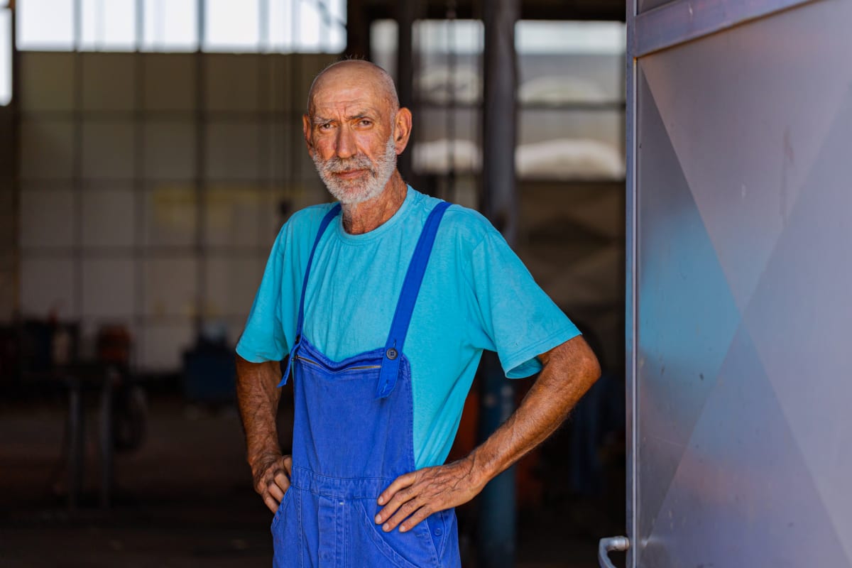 Full image of a person standing in a garage wearing work overalls.