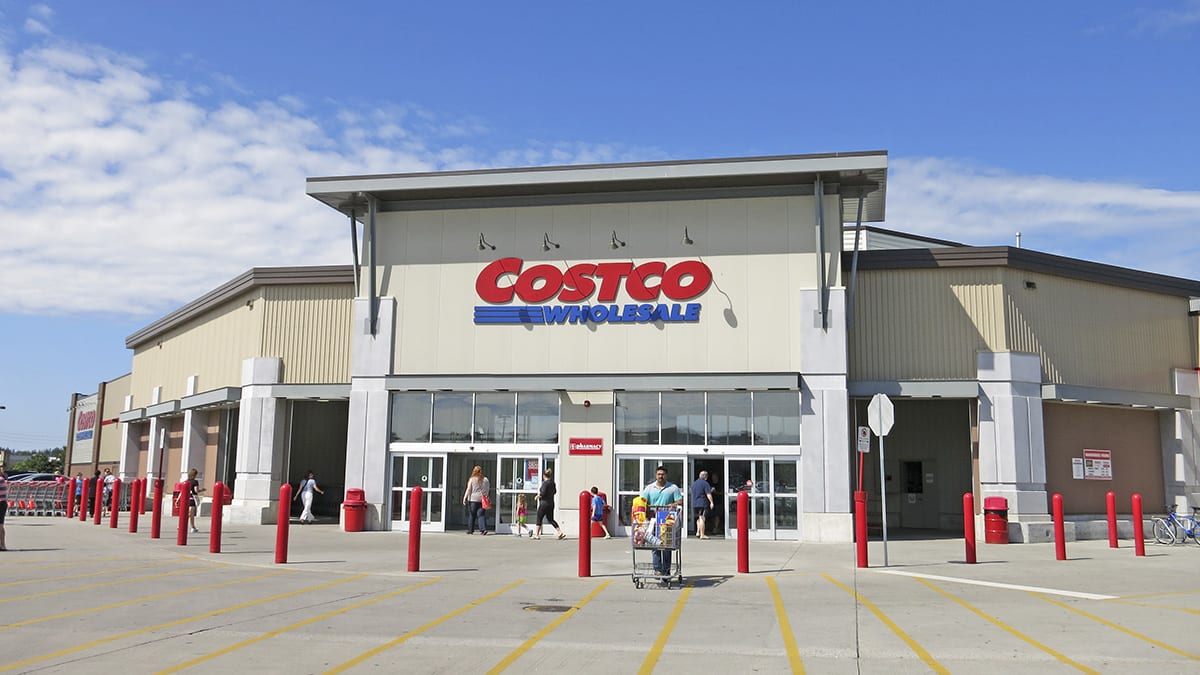 Exterior view of a Costco Wholesale store with people entering and exiting through the main entrance.