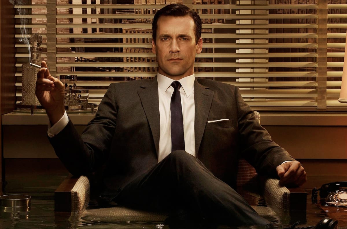 Don Draper in a suit sitting confidentally on a couch with a cigarette in his hand