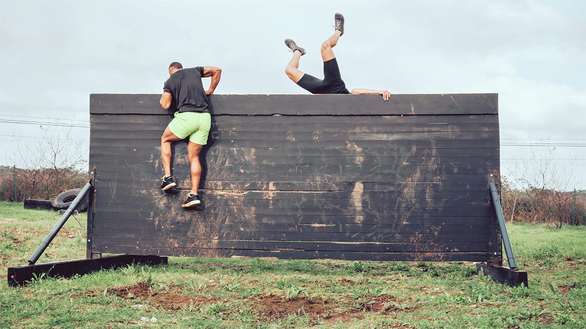 Two people going over a wall in an obstacle course.