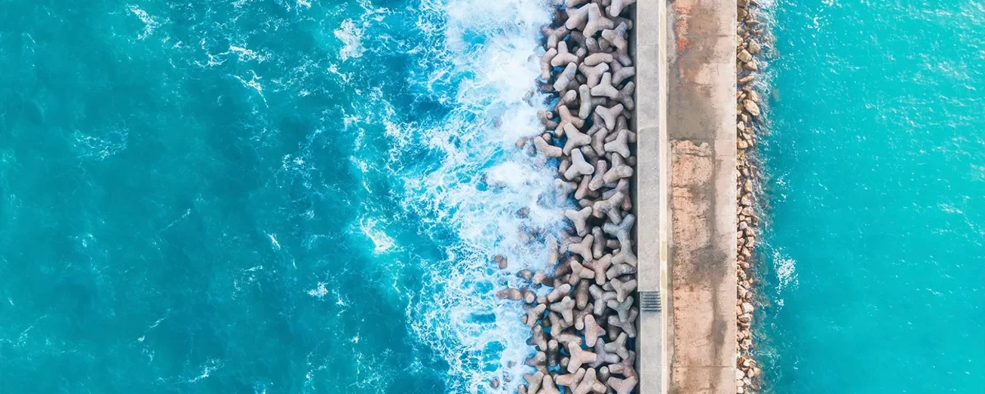 Bird's eye view of an ocean divided by manmade passage in the middle of it and enforced by large rocks