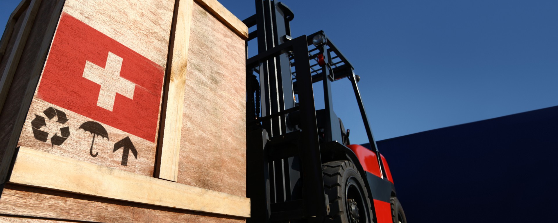 A tractor carrying a wooden crate with a Swiss cross on it.