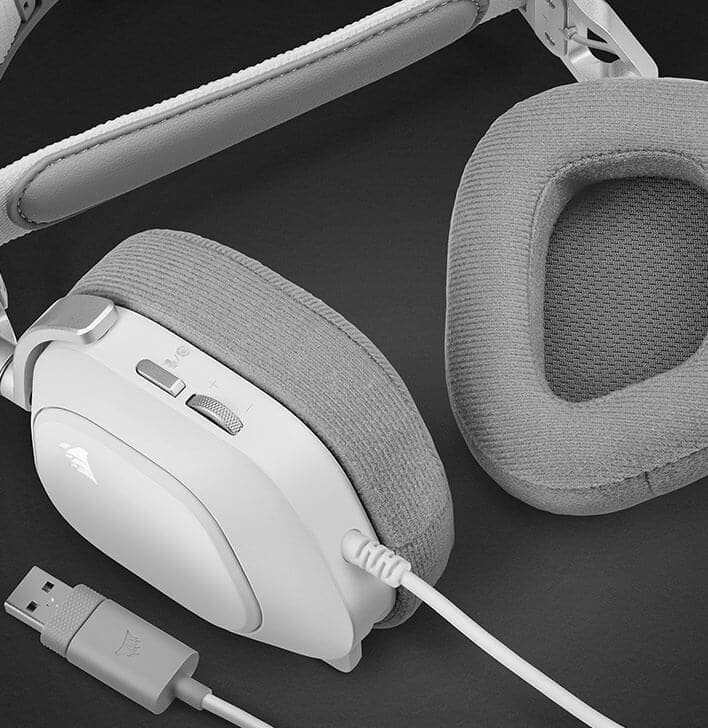 The HS80 RGB USB headphones are placed on a flat surface, with one of the earcups flipped over to reveal the memory foam ear pads.