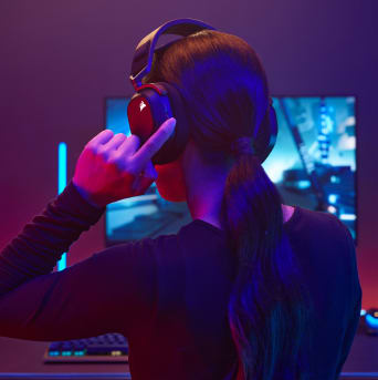 A female model is reaching toward the left ear cup to adjust volume controls on the black HS80 RGB WIRELESS gaming headset.