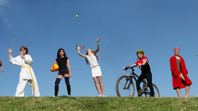 Sportliche Kinder stehen auf einem Hügel und wollen loslegen. Sie tragen Sportkleidung und Equipment, die sie für ihre Sportart brauchen. | Spiele.de