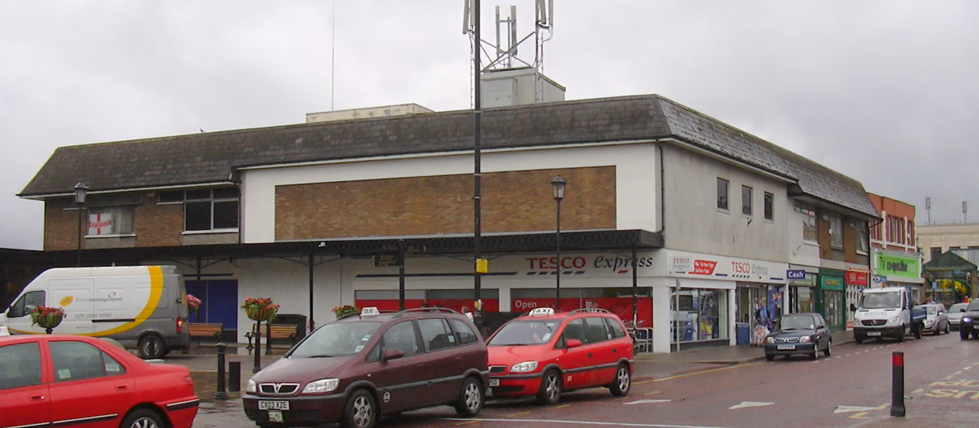 Street corner with a Tesco Express and parked cars.