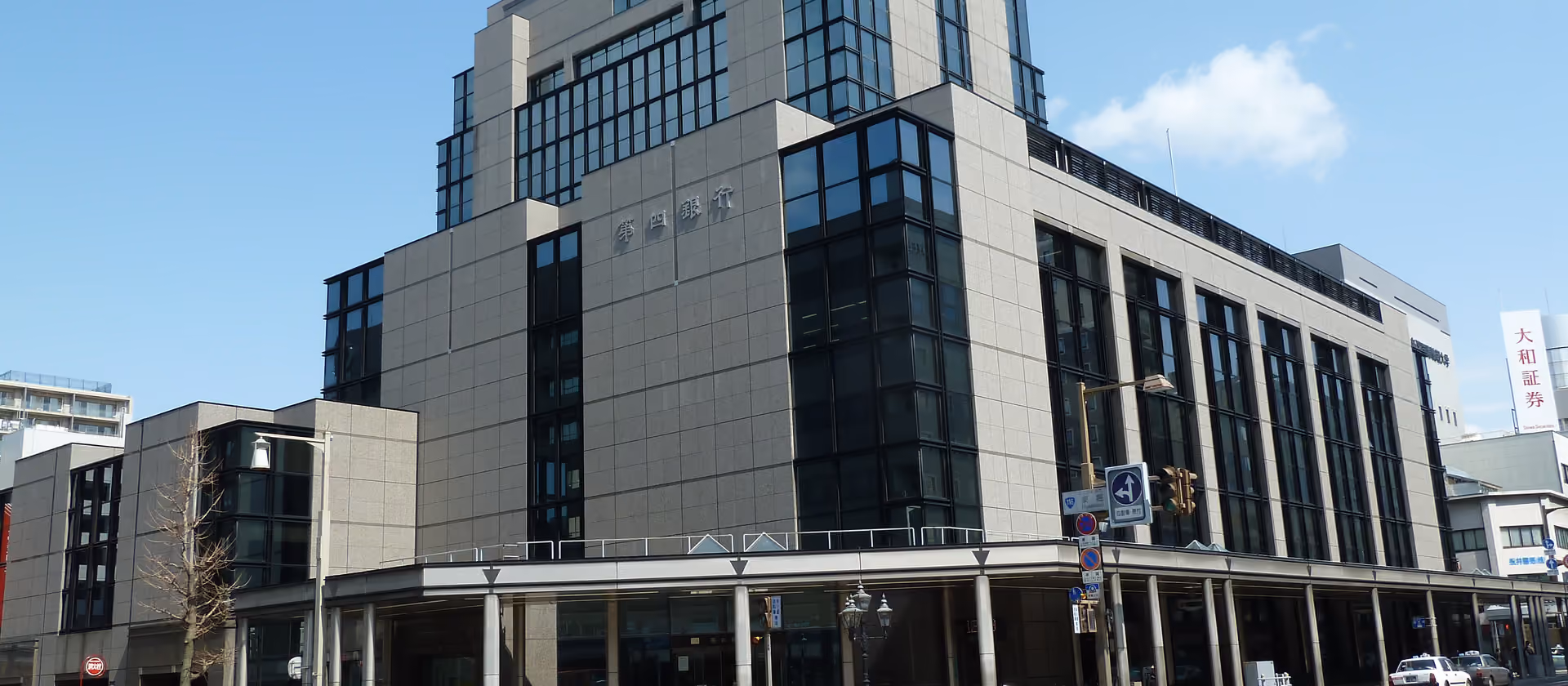 Modernes Bürogebäude an einer sonnigen Straßenecke unter blauem Himmel.