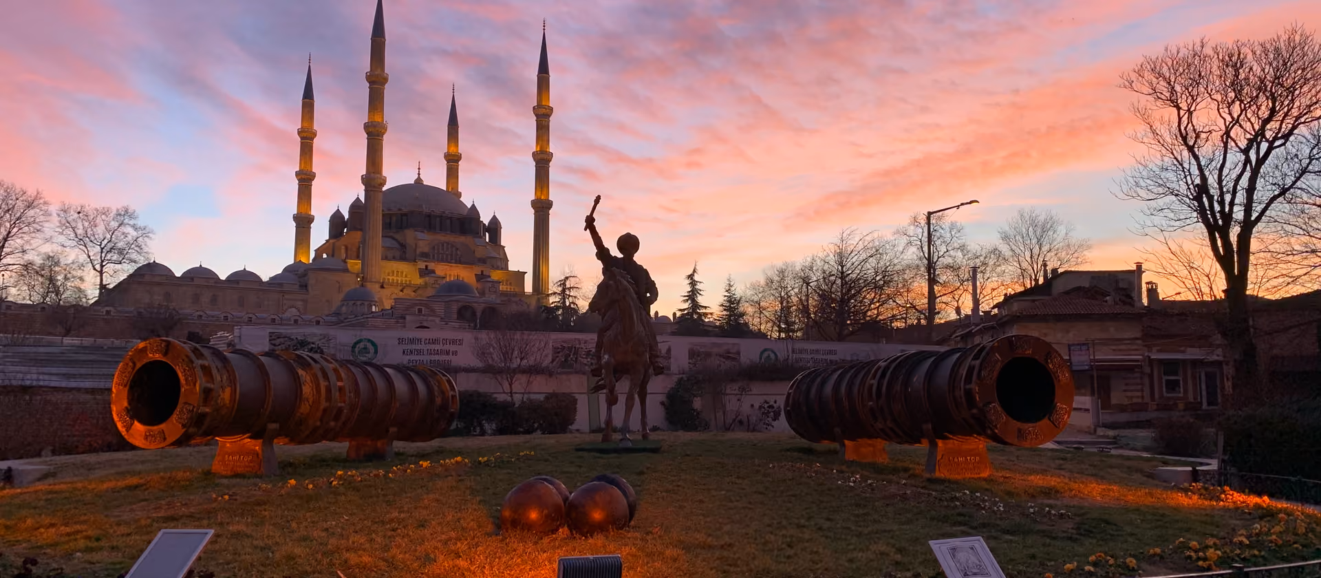 Eine Moschee mit vier Minaretten bei Sonnenaufgang, davor ein Reiterdenkmal und alte Kanonen.