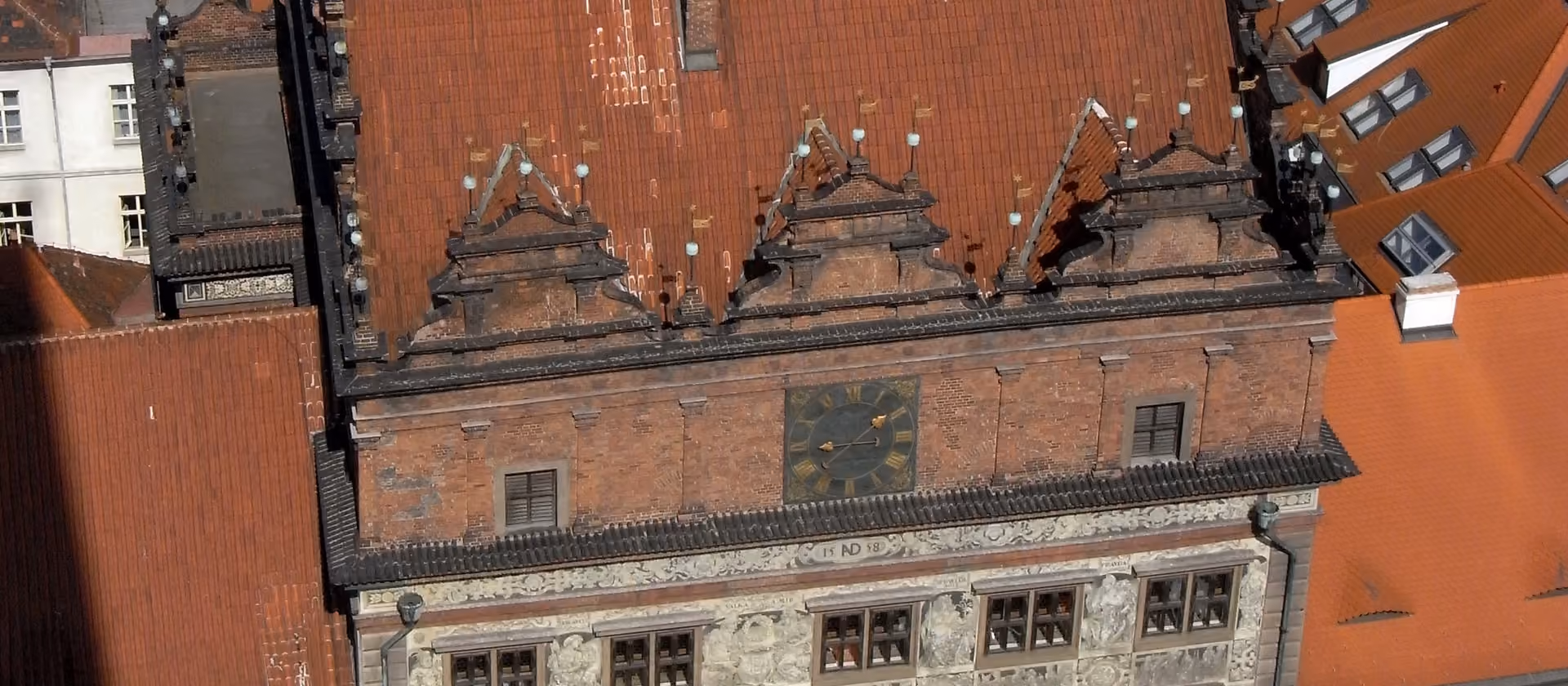Historisches Gebäude mit rotem Ziegeldach und Uhr in einer Altstadtstraße.