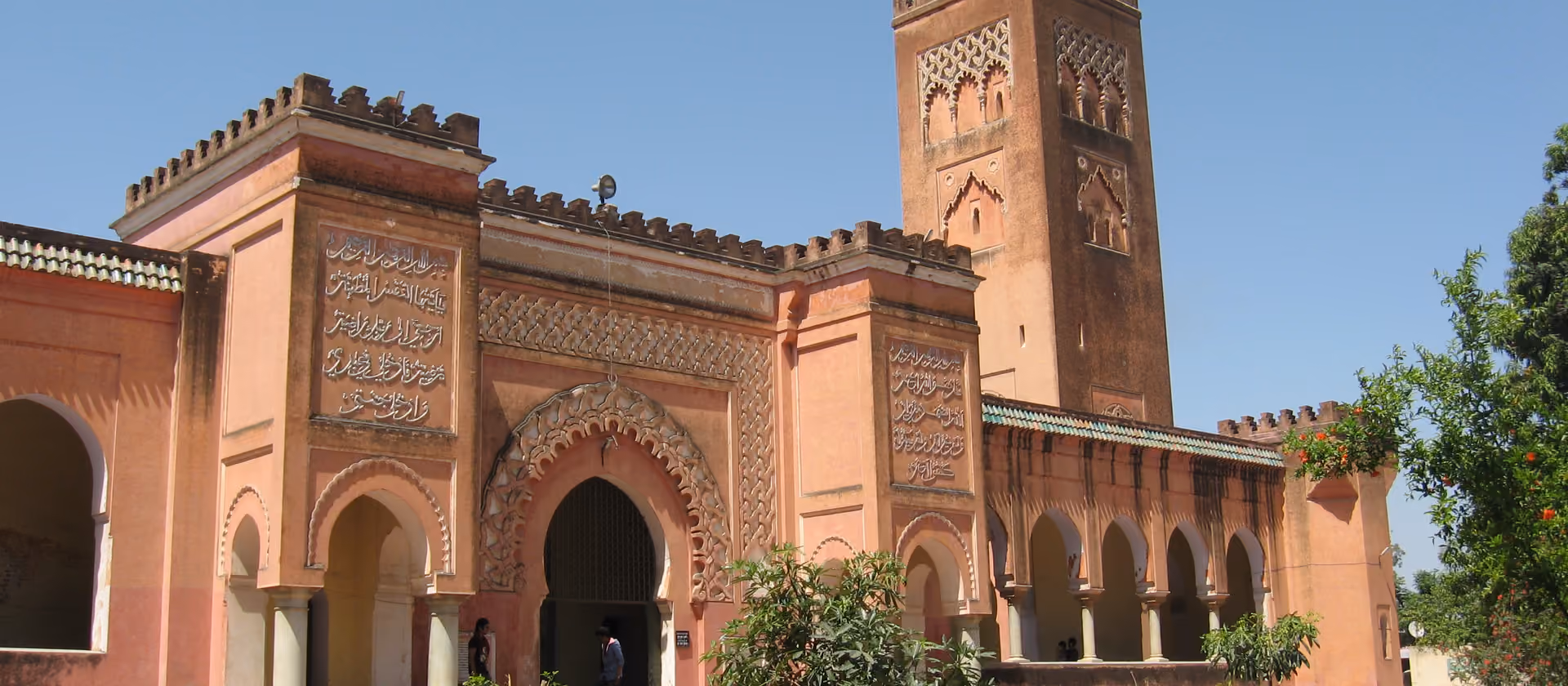 Außenansicht einer roten Moschee mit Minarett und Innenhof.