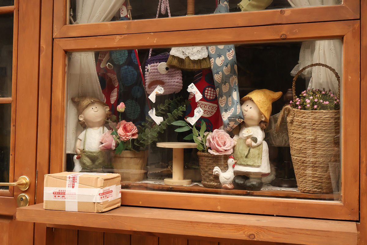 A wooden shop window with dolls and flowers