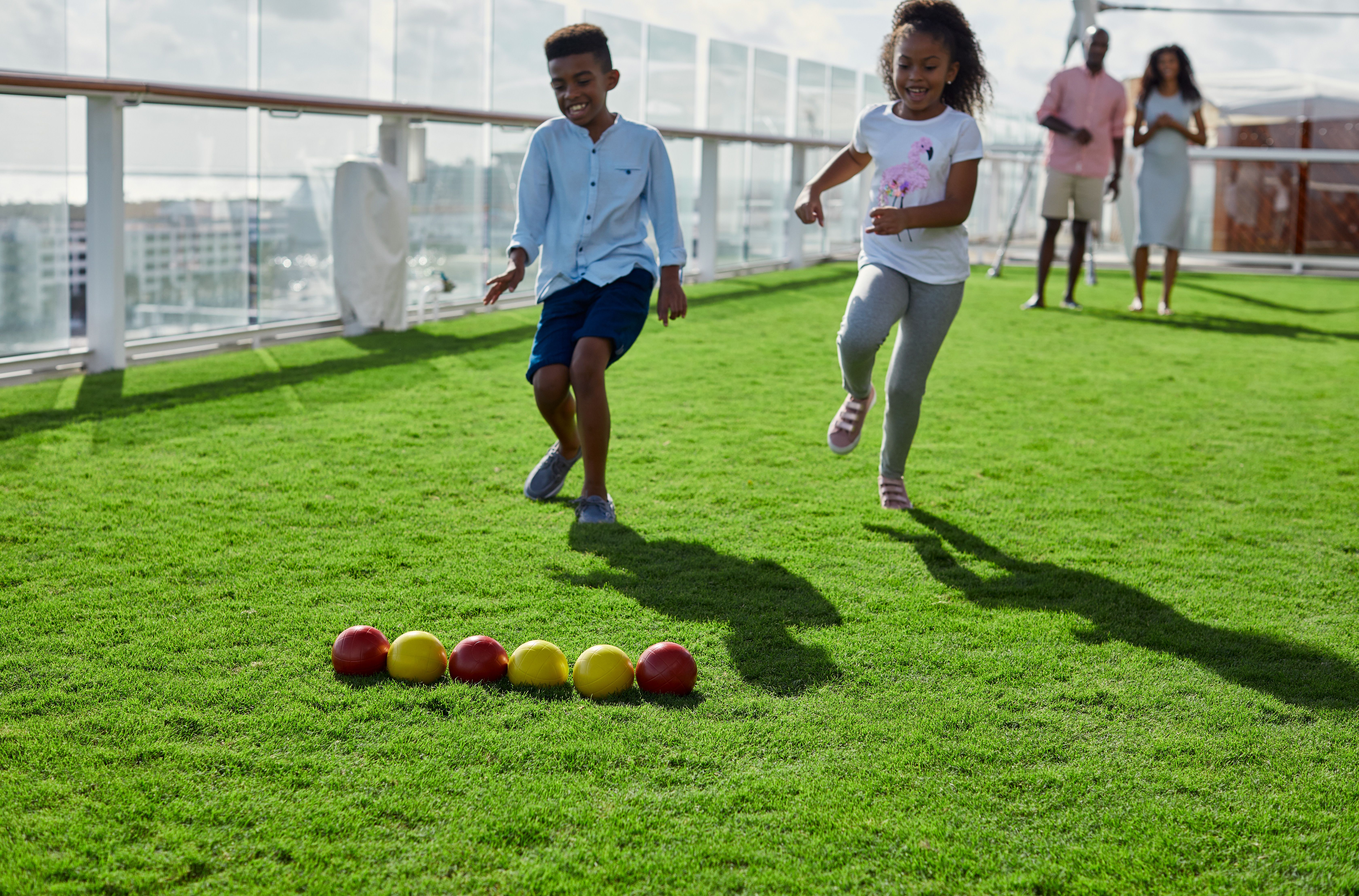 Kids joyfully playing bocce ball on the real grass of the Lawn Club aboard a Celebrity cruise ship.
