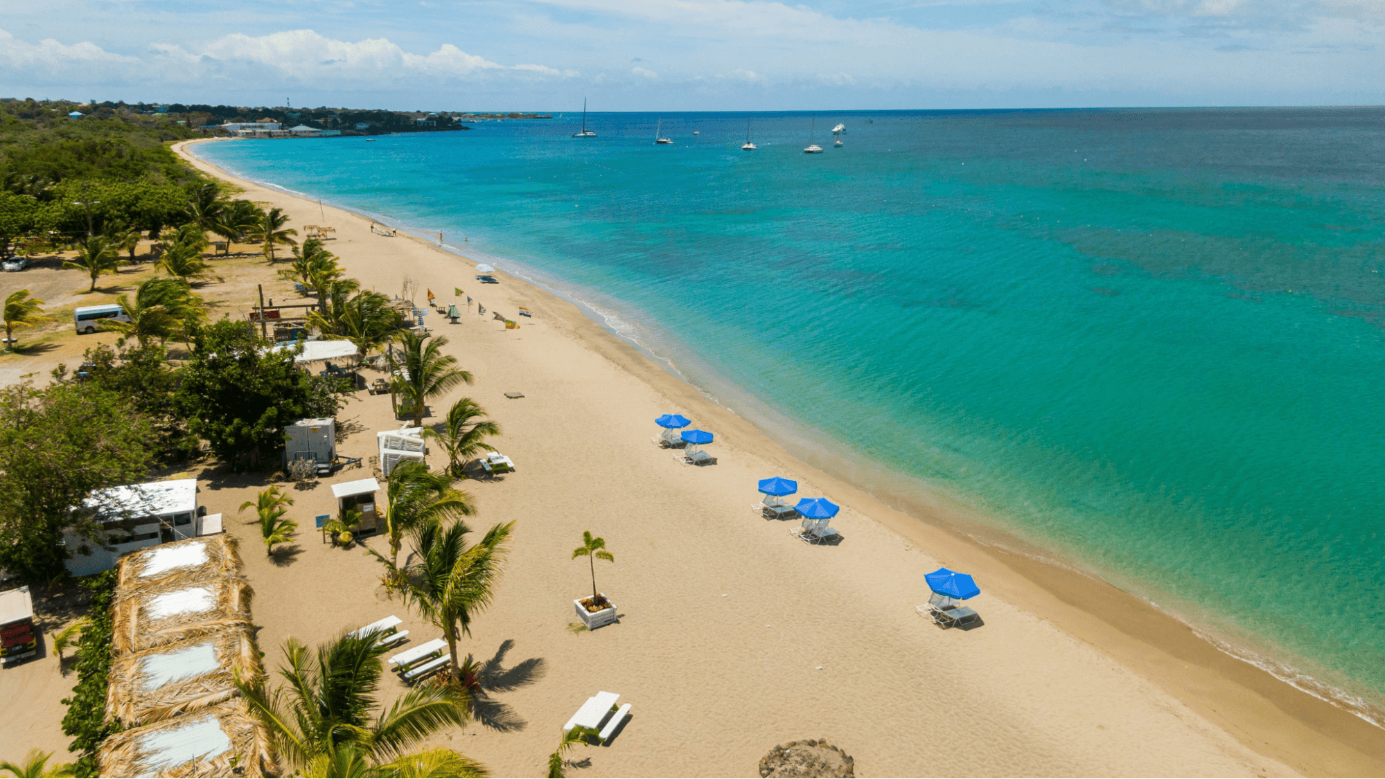 Aerial view of Pinney's St. Kitts beach with turquoise waters, golden sand, and lush green hills in the background.