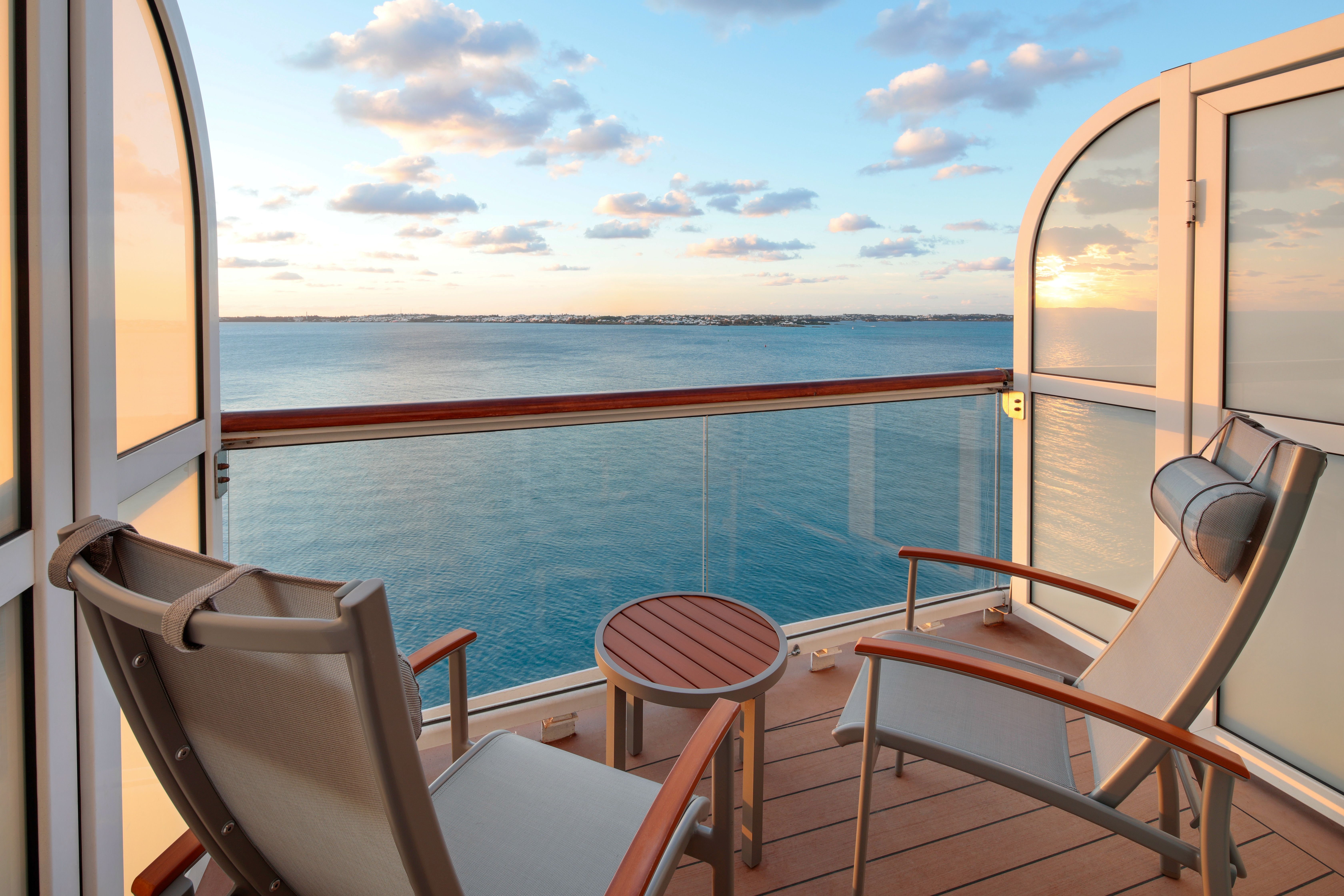 Aqua class balcony stateroom on Celebrity Summit featuring comfortable outdoor seating and expansive ocean views at sunset.