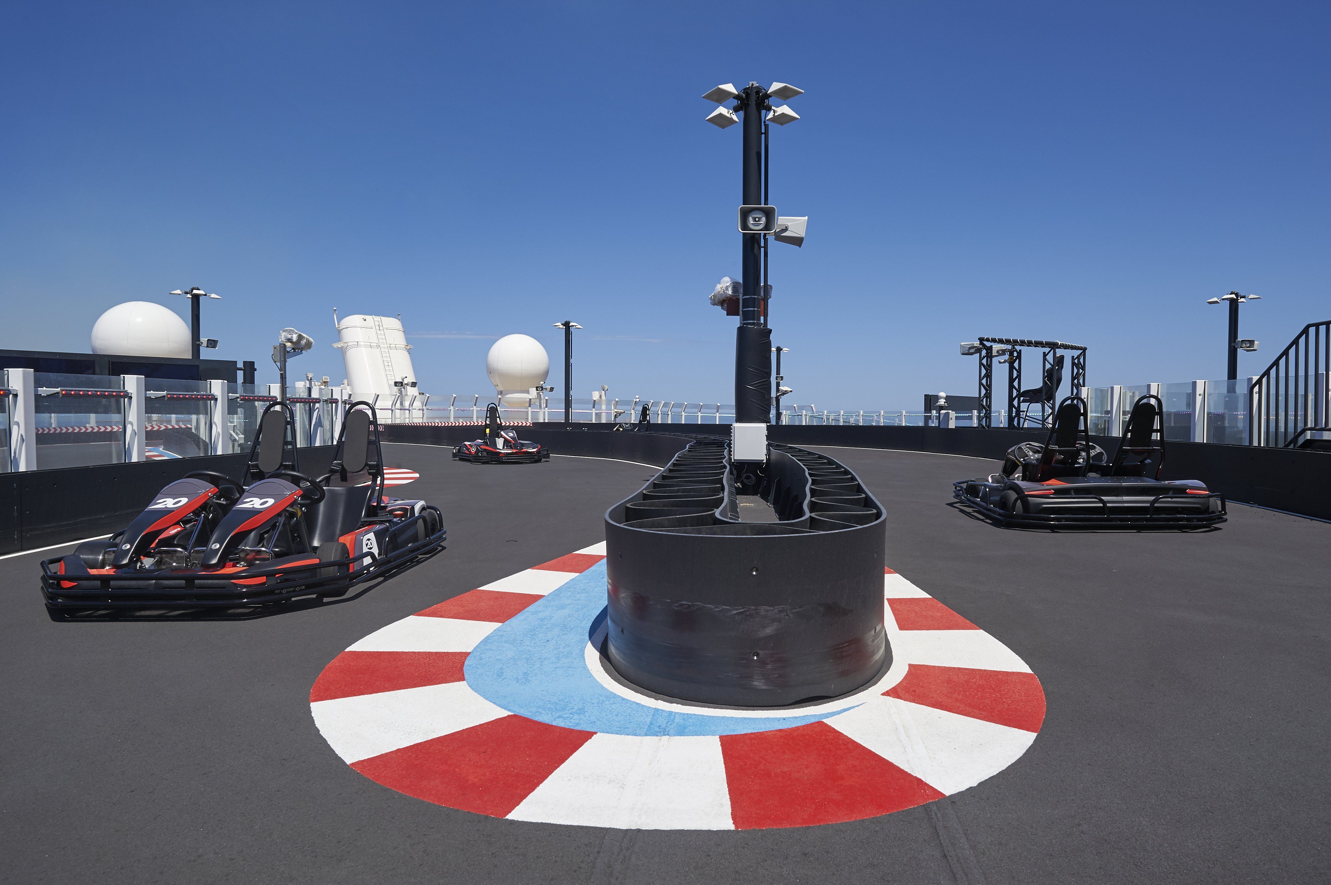 Racers ready on Norwegian Joy's speedway, a unique go-kart track at sea with ocean views, under a clear blue sky.