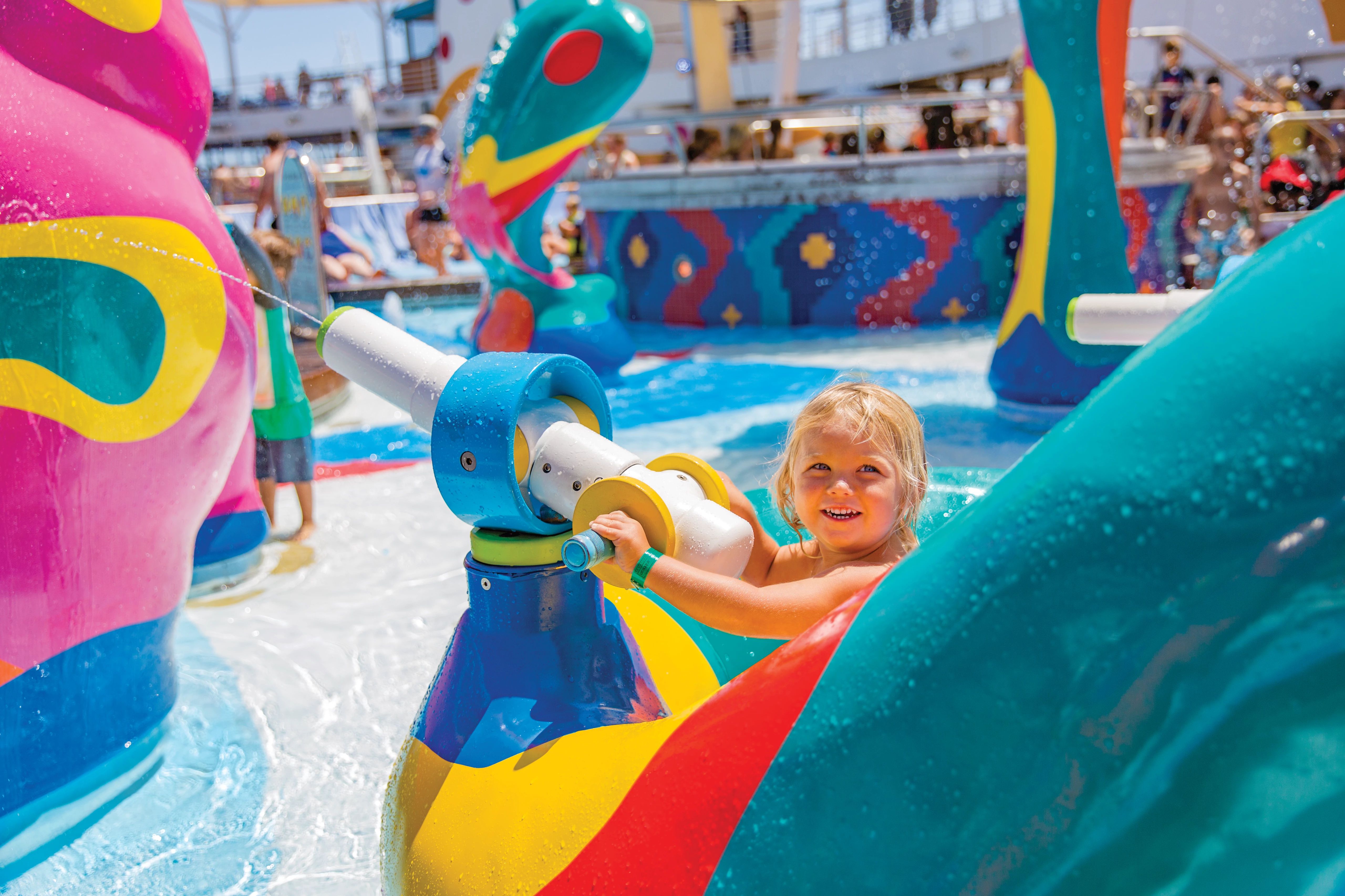 Alt text: "Delighted toddler playing with water cannons in H2O Zone on Royal Caribbean, colorful and lively children's water park on deck.