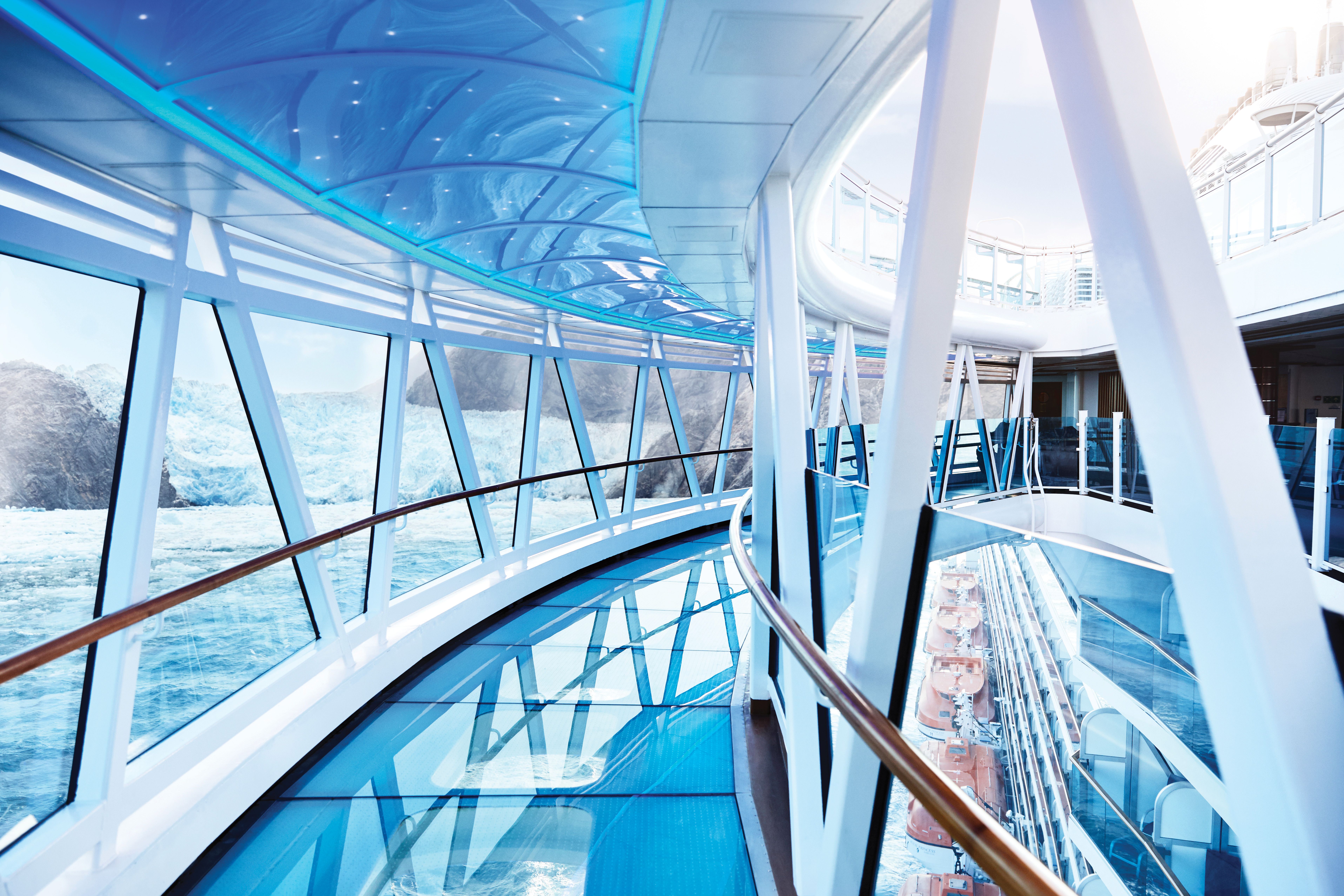 Passengers stroll on the SeaWalk, a glass-bottomed walkway on the Royal Princess, offering panoramic views of the sea and cliffs.