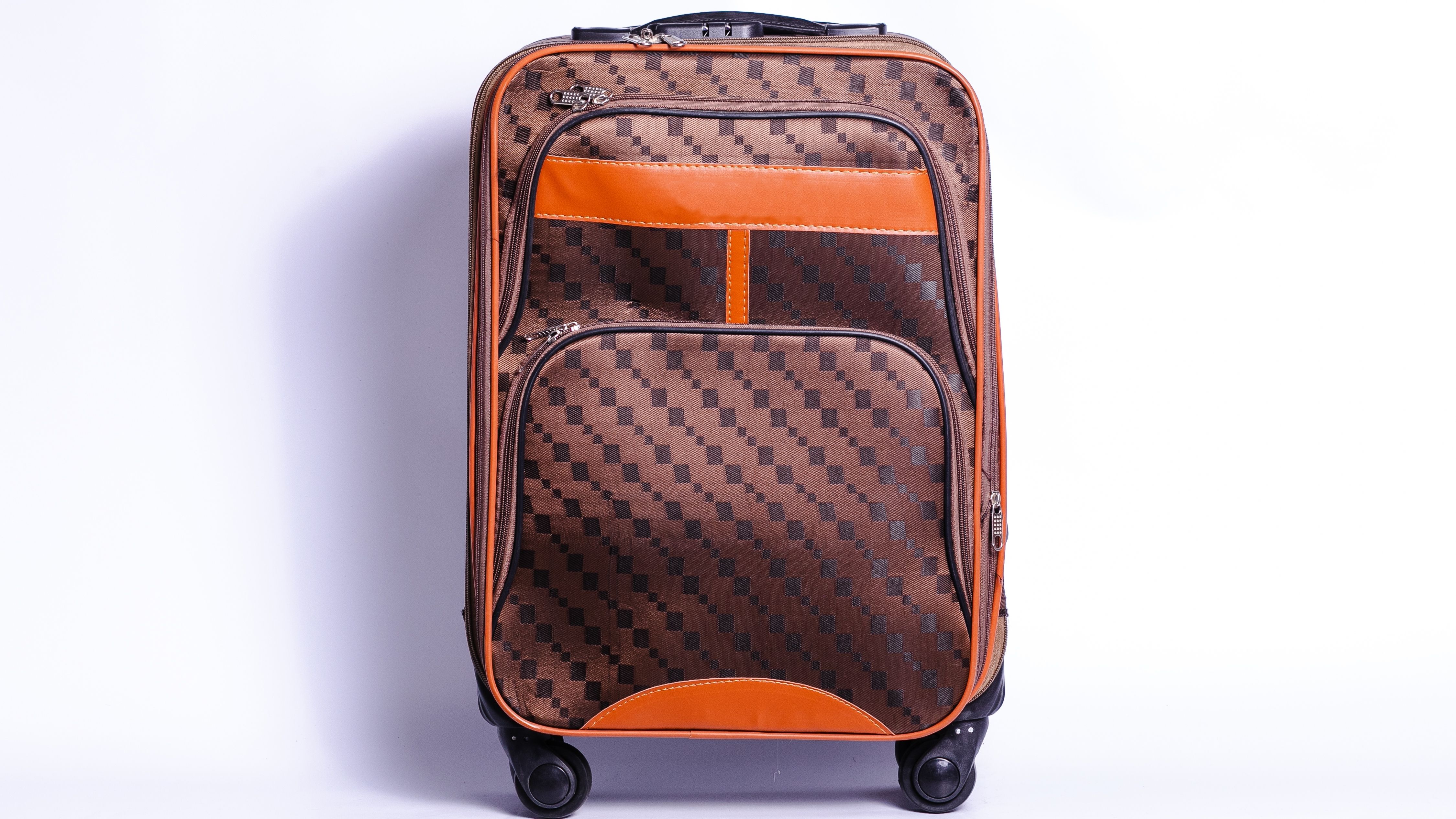 Designer soft sided luggage with a distinctive brown checkered pattern and orange accents, equipped with wheels and an extendable handle.